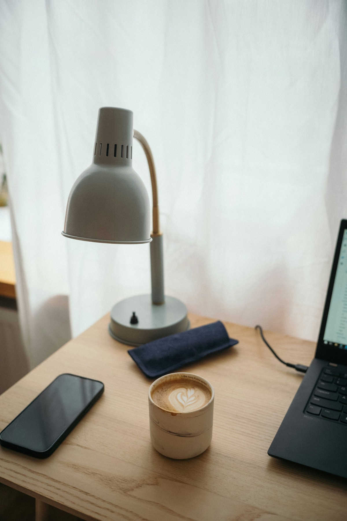 A calm desk with a lamp, a coffee, and an open laptop